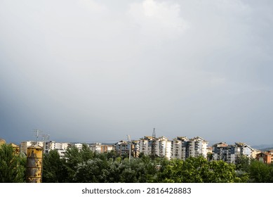 Dark dramatic storm clouds looming over residential city buildings and distant mountains