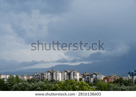Dark dramatic storm clouds looming over residential city buildings and distant mountains