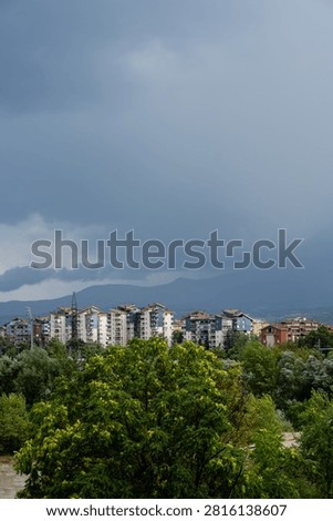 Dark dramatic storm clouds looming over residential city buildings and distant mountains