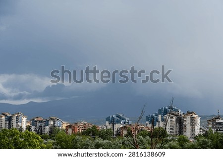 Dark dramatic storm clouds looming over residential city buildings and distant mountains