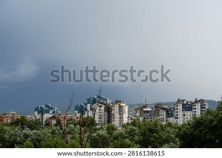 Dark dramatic storm clouds looming over residential city buildings and distant mountains