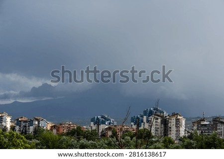Dark dramatic storm clouds looming over residential city buildings and distant mountains