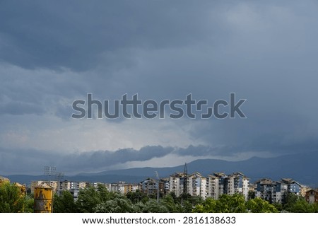 Dark dramatic storm clouds looming over residential city buildings and distant mountains