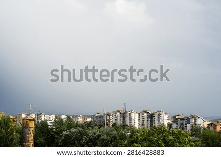 Dark dramatic storm clouds looming over residential city buildings and distant mountains