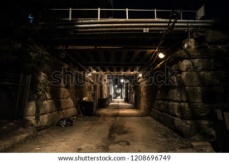 Dark and eerie urban city alley with vintage railway bridge and tunnel at night