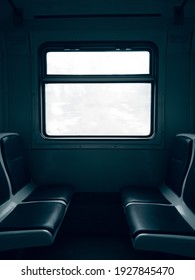 Dark Empty Cabin Of A Passenger Train Car With Seats And A Window In The Center Behind Which Is A White Sky.