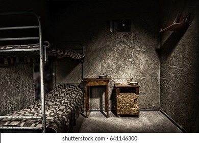 Dark empty jail cell with iron bunk bed and wooden bedside table with aluminum dishes