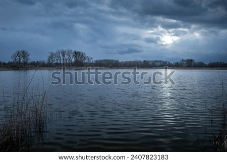 Dark evening clouds with glow from the moon over a calm lake, eastern Poland