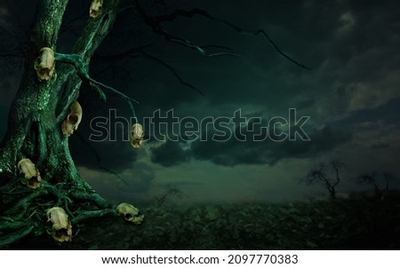 Dark fantasy landscape. Old dead tree and many skulls hanging on it. Crooked branches silhouettes on dramatic stormy cloudscape background