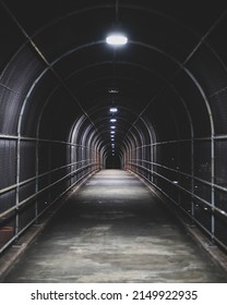 A Dark Fenced Walkway Is Illuminated By Overhead Lights