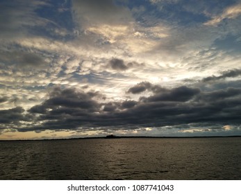 Dark floating gray storm clouds over the water with sunset sky