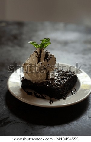 Dark food. Brownie fudge chocolate with cream ice cream and mint decoration on a white plate on a dark black textured background
