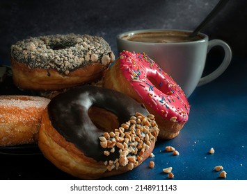 Dark food photography, doughnuts on a  black plate over a blue table with a cup of hot drink coffee chocolate moka. Dark food photography. Black background horizontal side view macro photography.