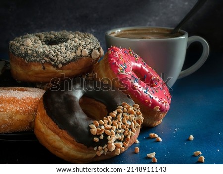 Dark food photography, doughnuts on a  black plate over a blue table with a cup of hot drink coffee chocolate moka. Dark food photography. Black background horizontal side view macro photography.