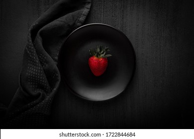 Dark food photography - A strawberry on a black plate with dark background and props 