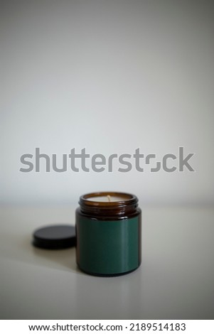 dark glass jar with a dark green or green empty label on a white background. open jar with a candle close-up.