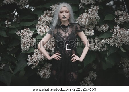 Dark goth girl standing in the forest, portrait of a wiccan witch performing magic