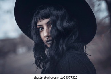 Dark gothic witch in black attire walking in the woods