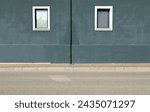 Dark gray plaster wall with gutter in the middle and two windows by sides. Sidewalk and street in front. Background for copy space.