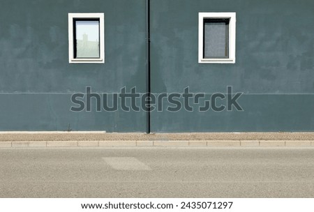 Dark gray plaster wall with gutter in the middle and two windows by sides. Sidewalk and street in front. Background for copy space.