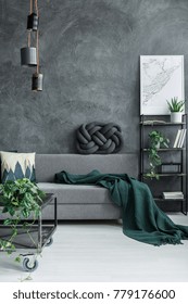 Dark Green Blanket On Grey Sofa Against Concrete Wall In Guy Room Interior With Designer Lamp And Map Poster On The Wall