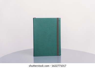 Dark Green Book, Agenda Or Planner Standing On A Grey Surface And White Background. Book Template.