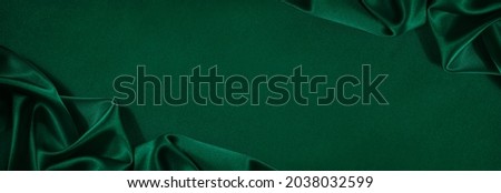 Dark green silk satin background. Beautiful soft folds on the smooth surface of the fabric. Luxury background with copy space for design. Wide banner. Top view. Flat lay.Birthday, Christmas, Valentine