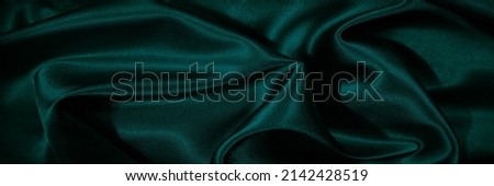    Dark green silk satin. Shiny silky surface of the fabric. Wavy folds. Elegant background with space for design. Web banner. Valentine, Christmas, holiday background.                            