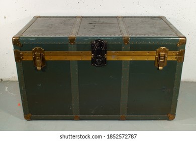 Dark Green Steamer Trunk. On A Grey Painted Floor. In Front Of A White Concrete Wall.