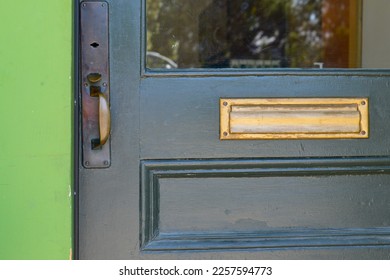 A dark green wooden door with half glass pane window, and a wooden panel. The vintage door has a brass door handle, a keyhole, and a letter plate. The trim of the building is vibrant green color.  - Shutterstock ID 2257594773