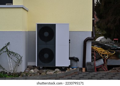 Dark grey colour air source heat pump installed outside the house painted grey and pastel yellow for heating and cooling homes. They work by moving outdoor heat indoors, or vice versa. 