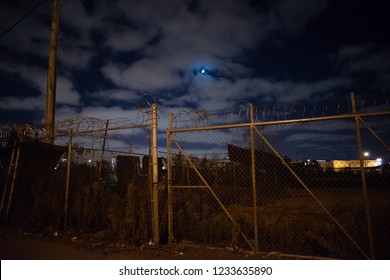 Dark and gritty rusty barbwire fence gate by an abandoned empty urban city lot with the moon at night - Powered by Shutterstock