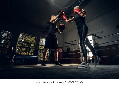 In the dark gym on the ring experienced trainer and young woman has a kick boxing fight. - Powered by Shutterstock