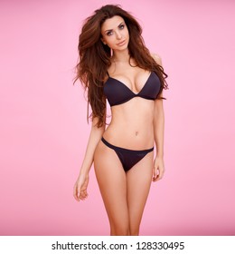 Dark haired beauty in a sexy black bikini  posing before a pink background