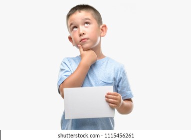 Dark haired little child holding a blank card serious face thinking about question, very confused idea