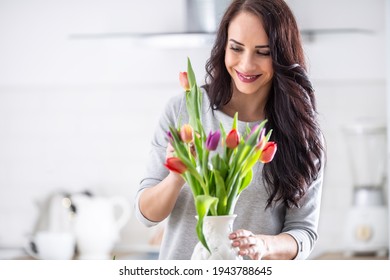 Dark haired woman happily putting fresh colorful tulips into white vase. - Powered by Shutterstock