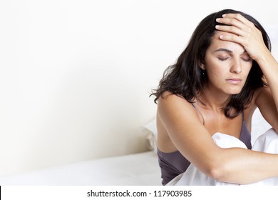 Dark Haired Woman With Headache Sitting On Her Bed