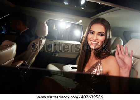 Dark haired young woman waving from the back of a limo