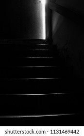 Dark Image In Black And White Of Stairs Leading Up From Cellar To A Door Ajar.