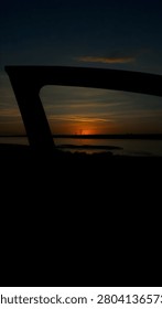 A dark interior silhouette frames a vibrant orange sunset over a body of water