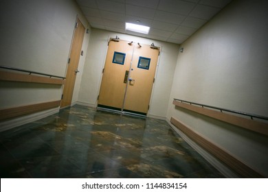 Dark & intimidating view of closed hospital doors at end of hallway.