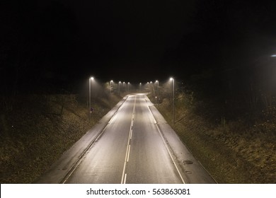 A dark lonely road in the night. With street lamps lightening up the road.