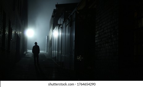 A Dark Male Figure Is Silhouetted Against A Foggy Urban Alleyway