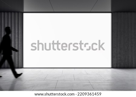 Dark man silhouette walking by big blank white screen with space for your logo or text in abstract empty hall area with dark ceiling and floor, mockup