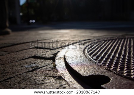 Dark manhole cover on urban sidewalk near sunset deep shadows and texture selective focus