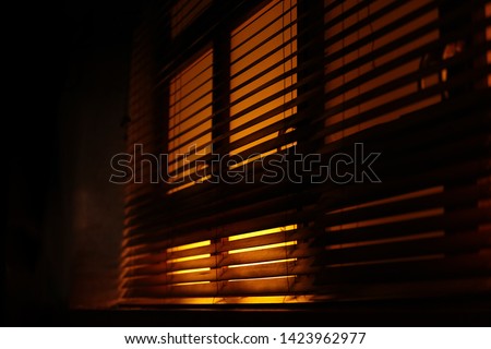 Dark, moody atmosphere set by yellow light softly piercing through the blinds. The shutters create a lovely contrast between light and shadow.Also a concept of mafia, fear, kidnapping, sleep, sunlight