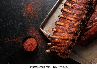 Dark and moody rack of meaty baby back ribs with spicy dry rib rub seasoning on a worn metal sheet pan