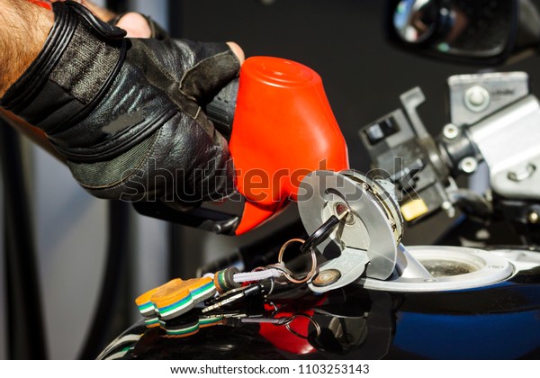 A dark motorcycle. In the tank a gun for fueling.\
Shallow depth of cut.