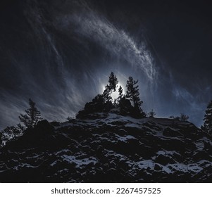 Dark mountain scape with the sun setting through a tree at the top