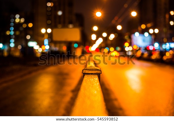 Dark\
night in the big city, pavement with billboard and the road. Close\
up view from the handrail on the sidewalk\
level